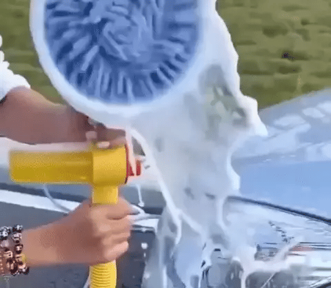 Spinning blue microfiber car wash mop on a yellow handle spraying foam onto a car