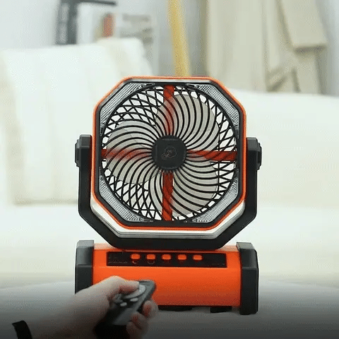 Orange 3-in-1 camping fan with light on a table, operated by a hand holding a remote