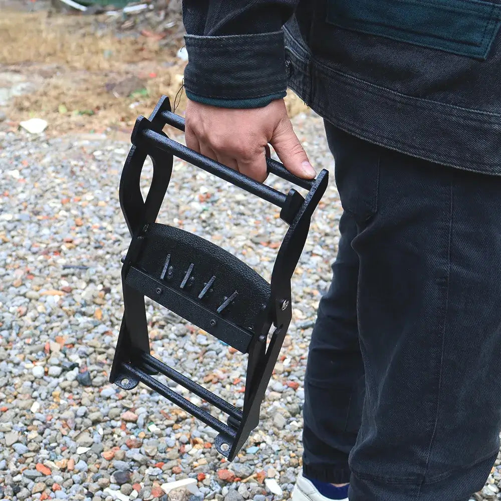 Hand carrying a compact black steel log splitter by its crossbar on a gravel ground