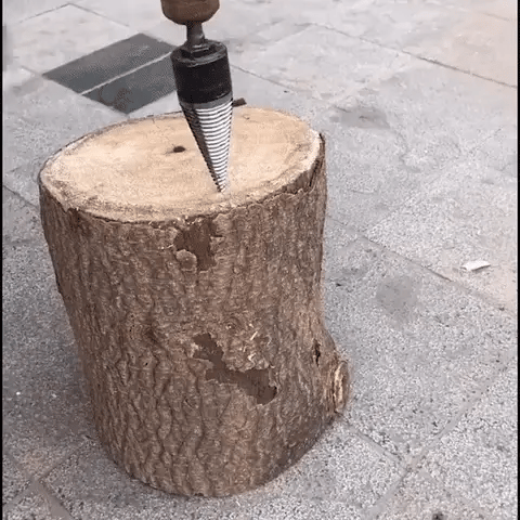 Cone-shaped splitter bit drilling into a wood stump on a paved patio