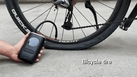 Hand holding a black portable air pump inflating a bicycle tire