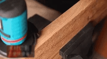 Close-up of a blue mini grinder working on the edge of a wooden board